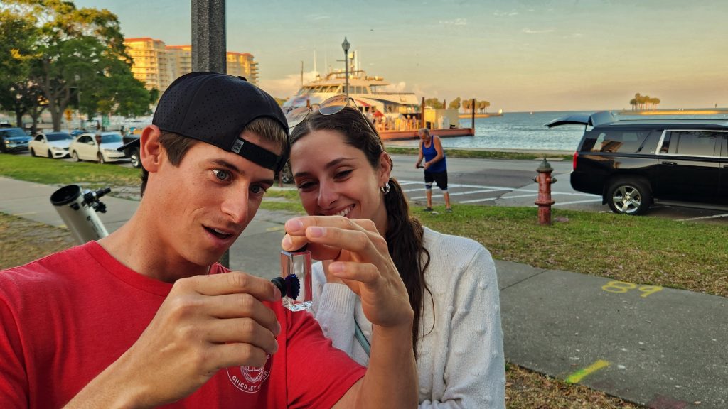 Situated on the sidewalk, Alex Martin demonstrates a small experiment to an excited and engaged young woman. 