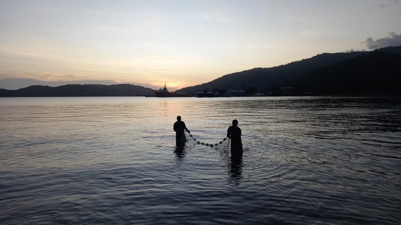 Joshua Prentice and a colleague holding a net between them while standing knee deep in a large body of water near sunset.